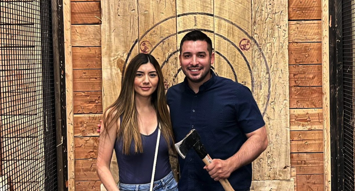 Happy couple standing in front of an axe throwing target holding an axe on a date night.